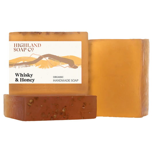 Three rectangular bars of Highland Soap Co. Whisky & Honey organic handmade soap arranged on a white background, with one bar showing its paper label and two bars showing the warm amber and honey-colored soap texture.