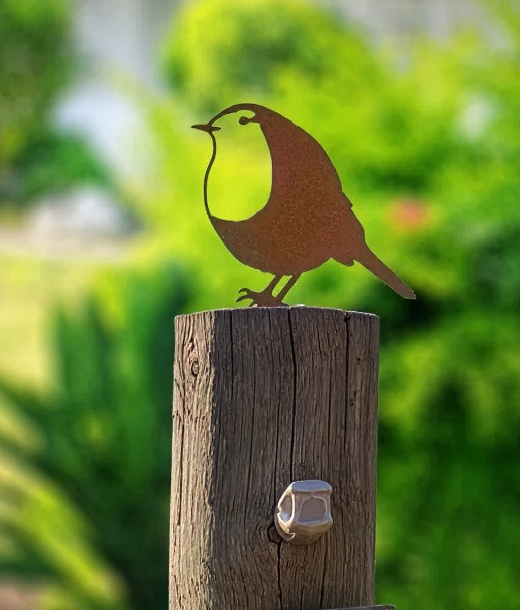Metal Robin fence topper sculpture on a wooden post with a blurred green garden background