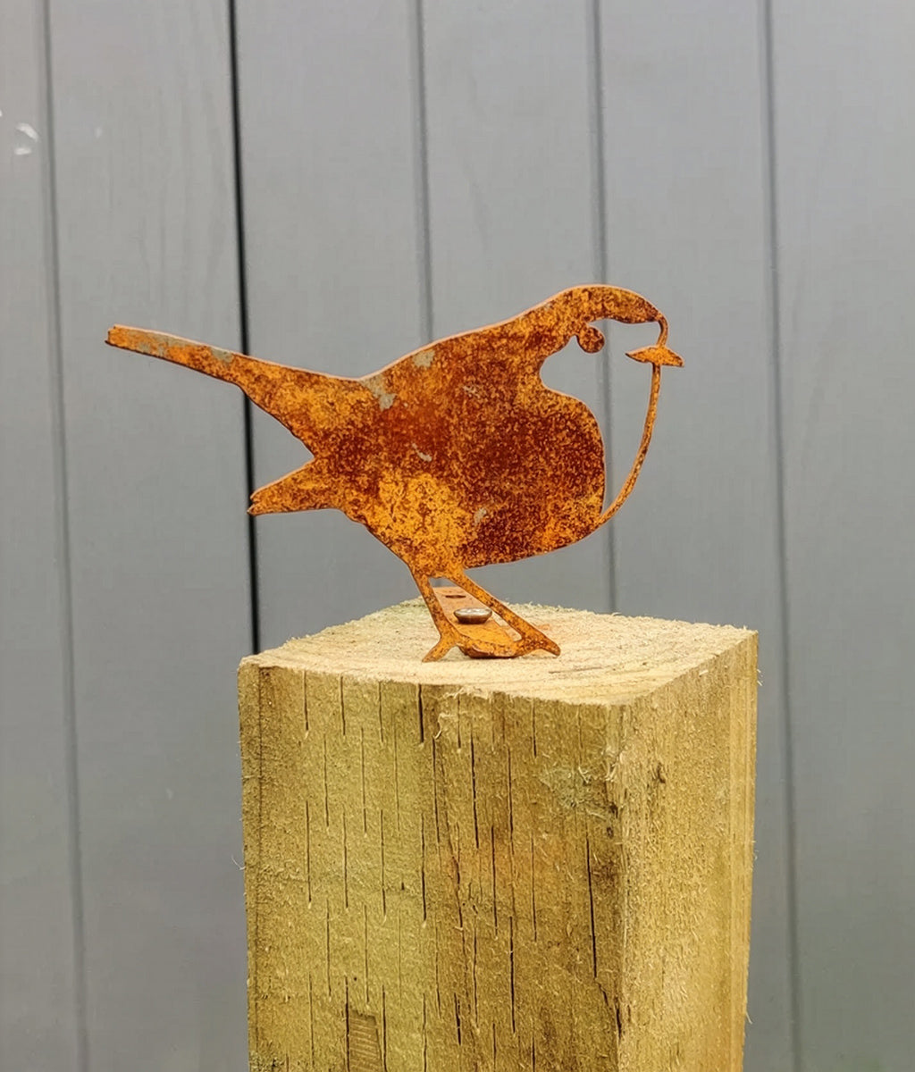 Rusted metal Robin fence topper  sculpture on a wooden post against a grey wall.