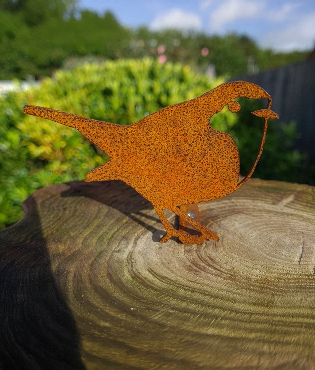 Rusted metal Robin fence topper  sculpture on a wooden log with greenery in the background
