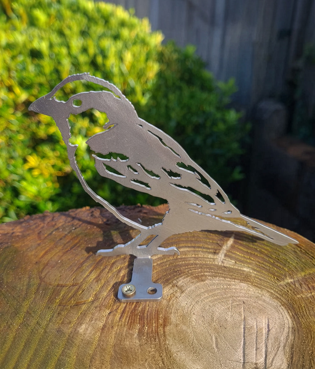 Metal Sparrow Fence Topper sculpture on a wooden log with greenery in the background