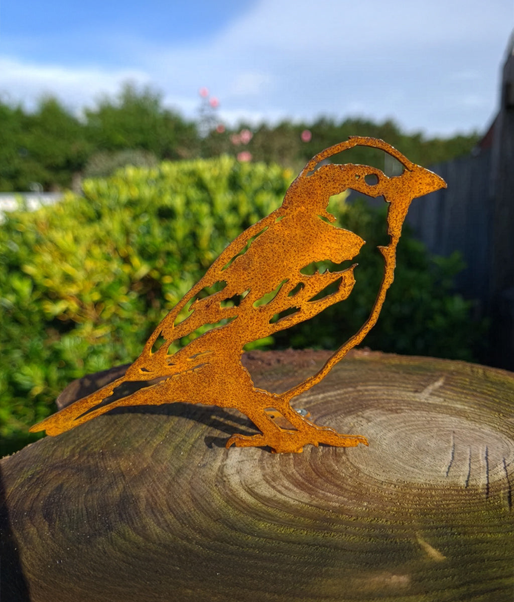 Rusted  metal Sparrow fence topper sculpture on a wooden log with a garden background