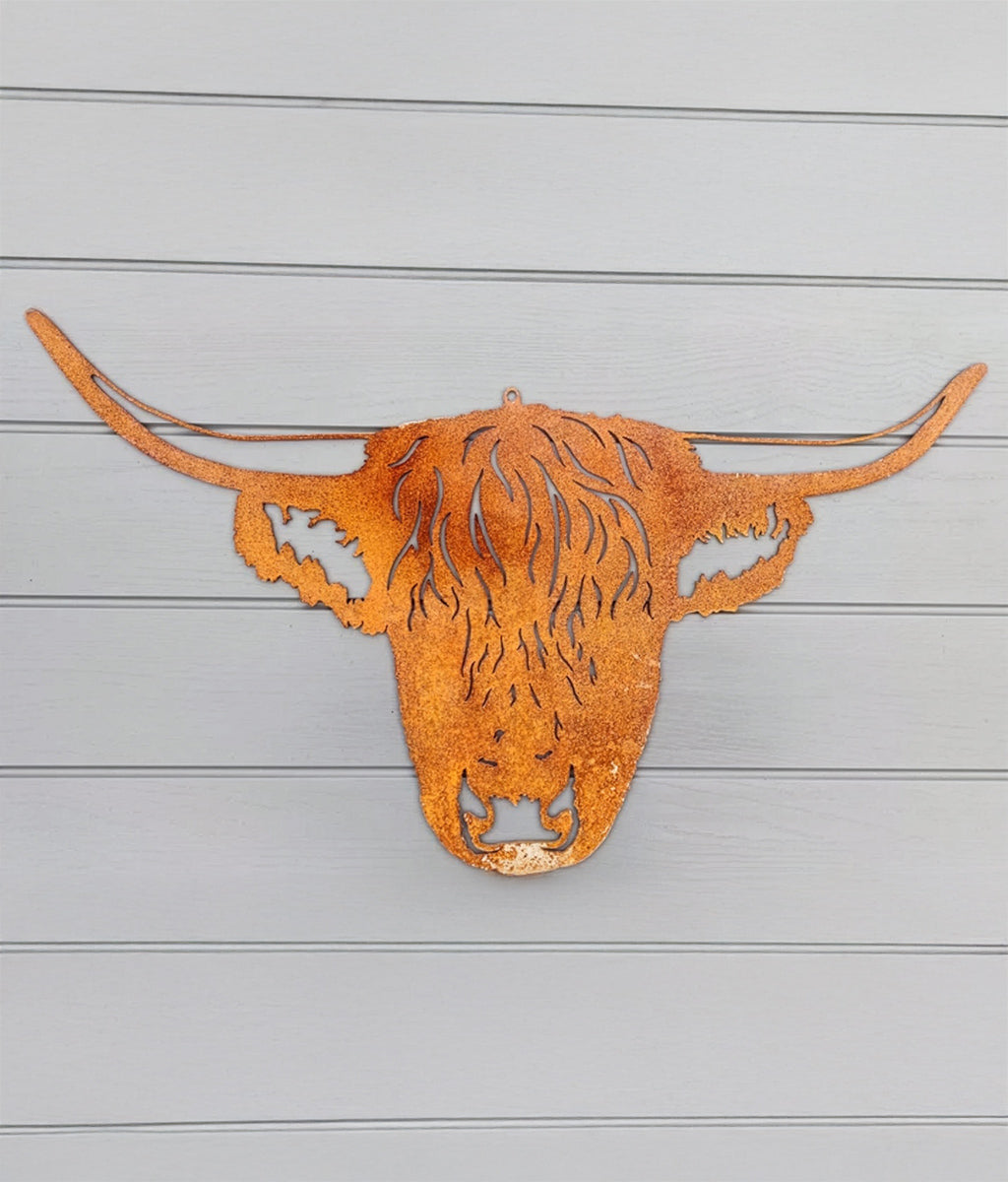 Rust-colored metal sculpture of a highland cow head on a wooden background