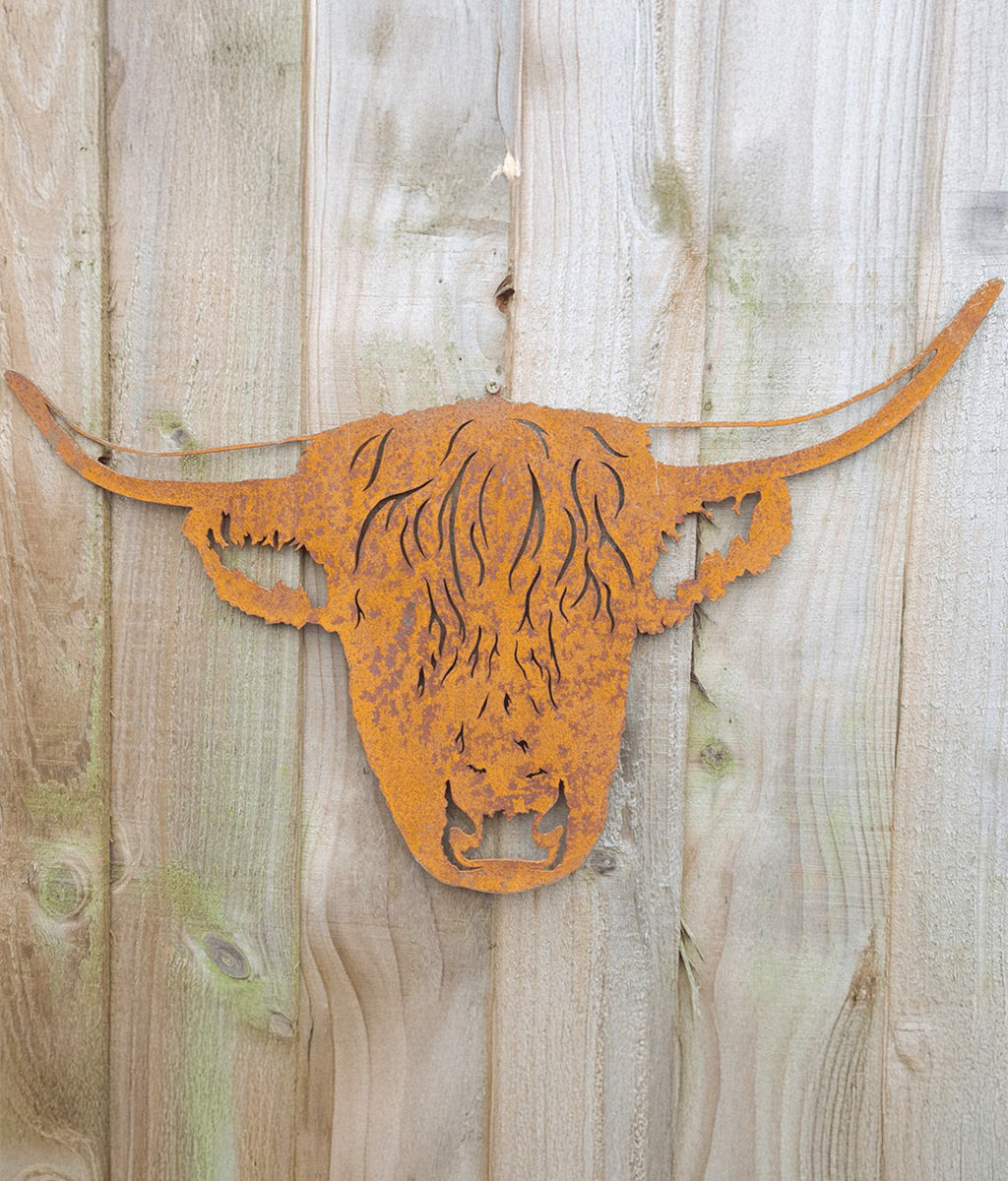 Rust-colored metal sculpture of a highland cow head on a wooden background