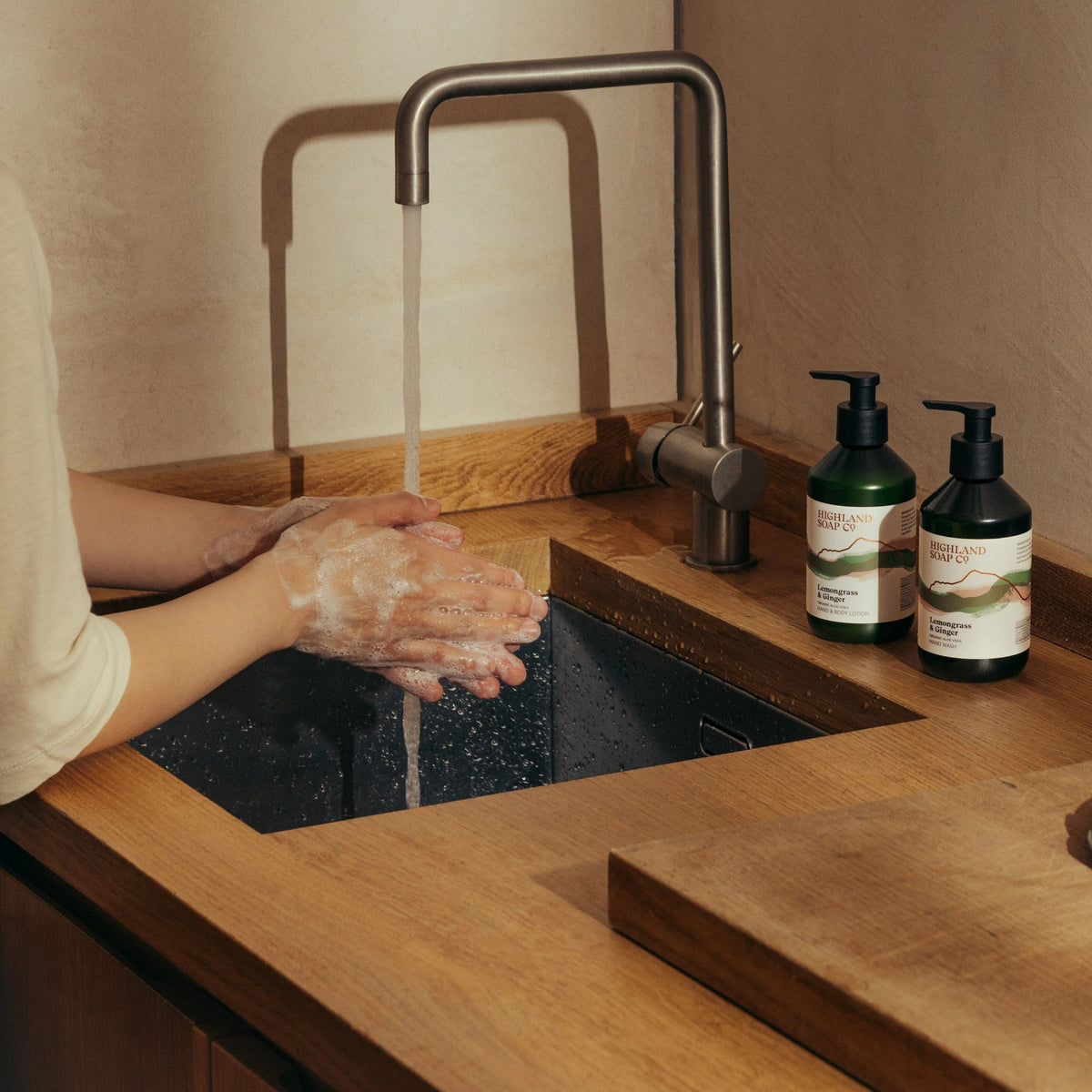 Person washing hands under a running faucet with Highland Soap Co, Hebridean Seaweed Hand Wash on a wooden countertop.