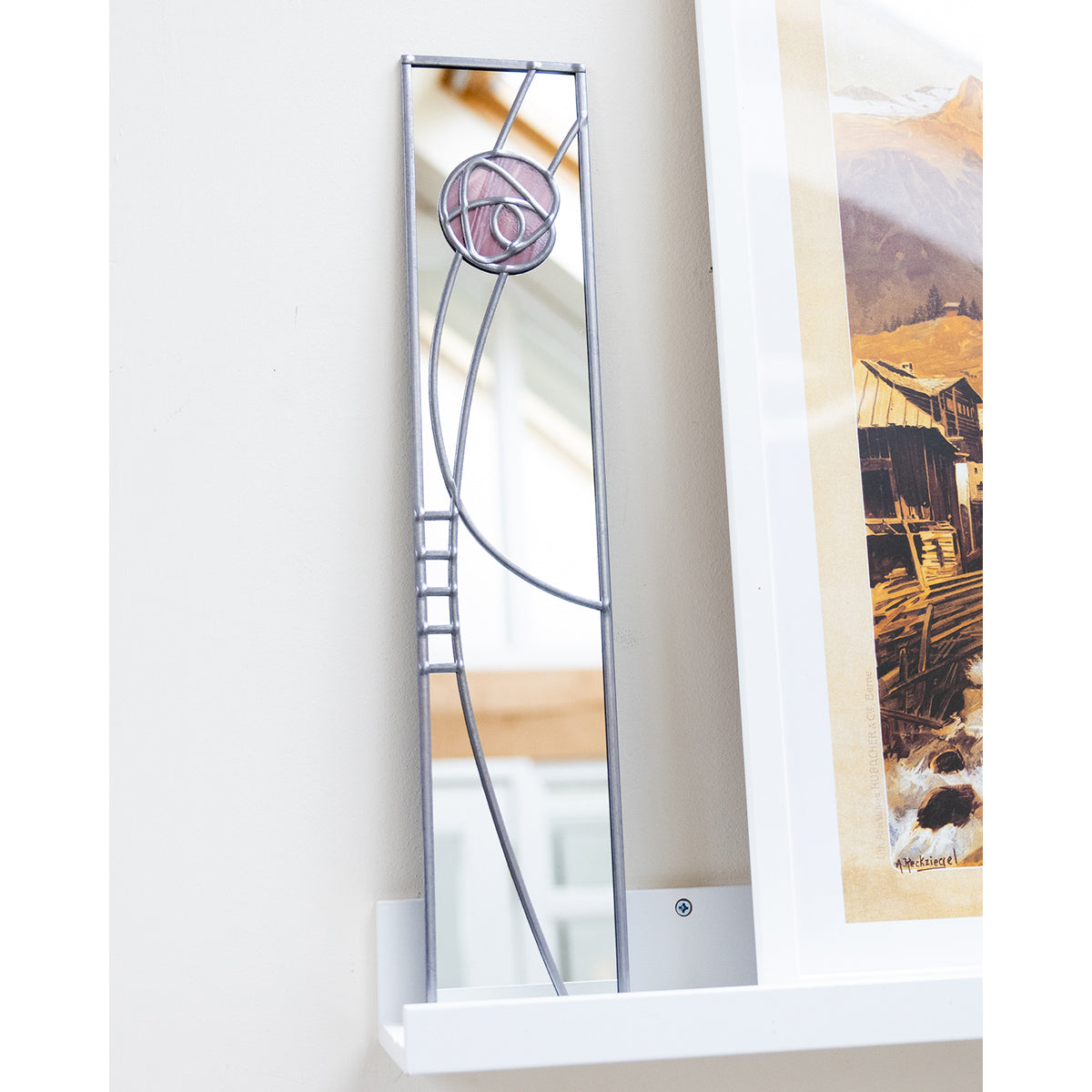 Decorative mirror with a unique design on a white wall next to a framed picture.