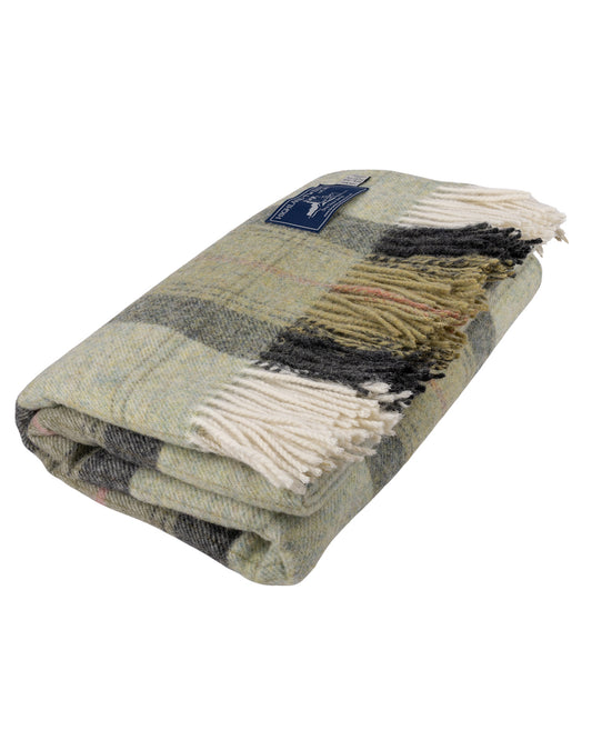 A folded Skye Green Pure New Wool Throw Blanket with cream fringe, featuring a mix of sage green, gray, black, and beige tones, with a small blue brand label.