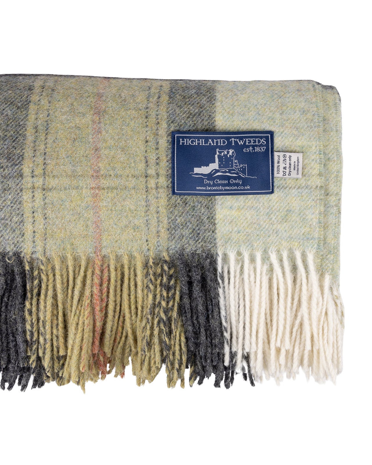 A folded Skye Green Pure New Wool Throw Blanket with cream fringe, featuring a mix of sage green, gray, black, and beige tones, with a small blue brand label.