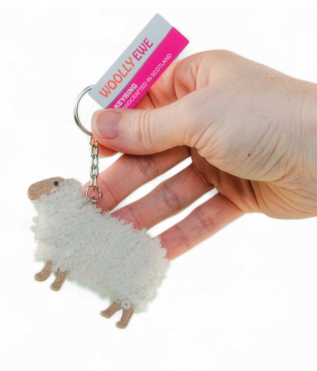 Hand holding a fluffy sheep keychain with a visible brand tag on a white background