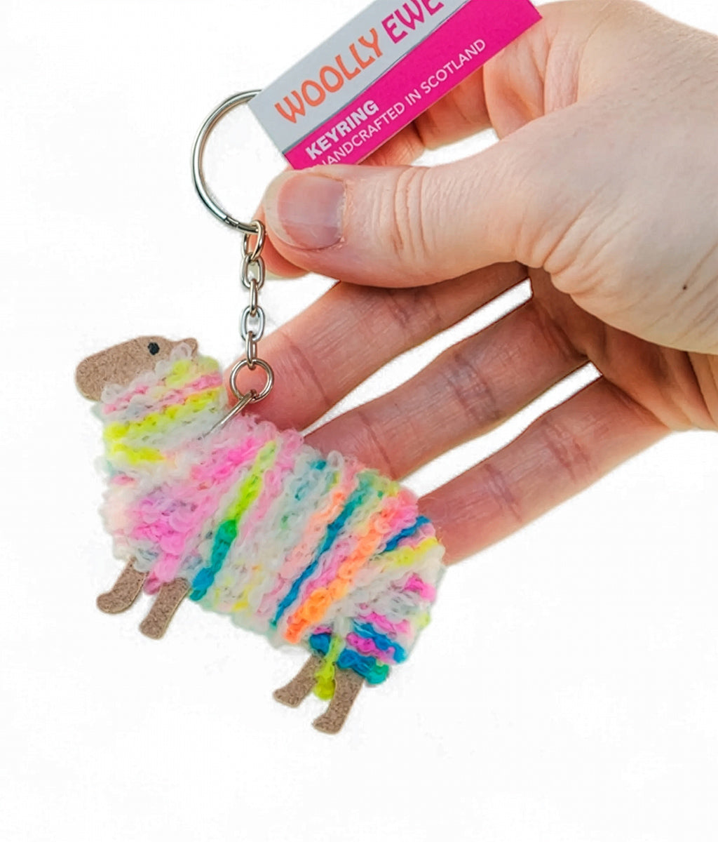 Colourful sheep keychain held by a hand with 'Woolly Ewe' branding.