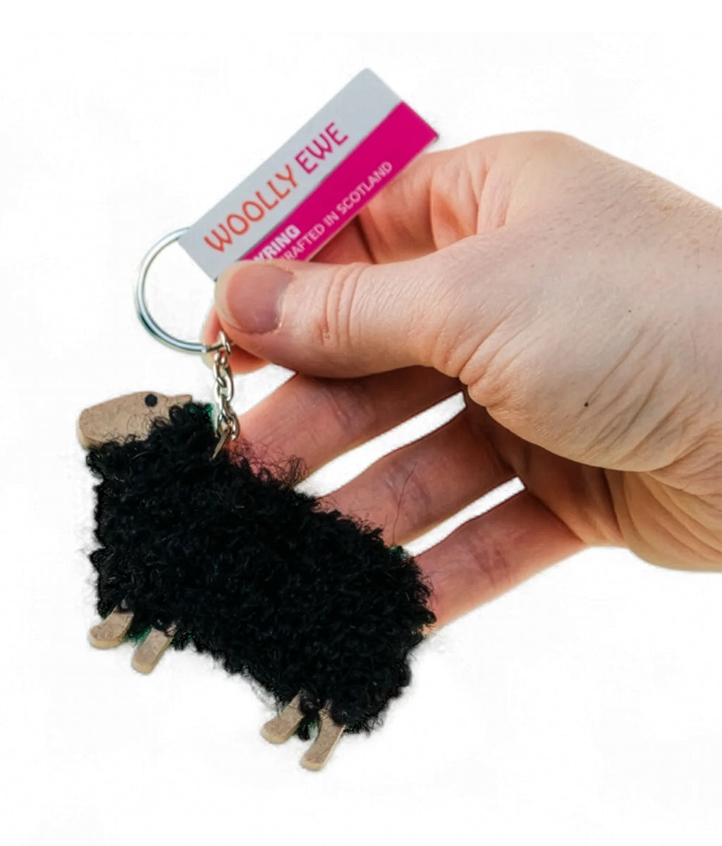 Hand holding a black sheep keychain with 'Woolly Ewe' packaging.