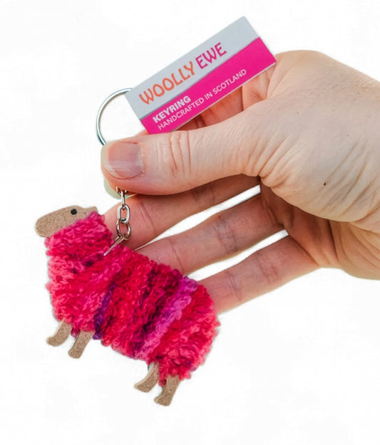 Hand holding a fluffy pink keychain with 'Woolly Ewe' branding on a white background