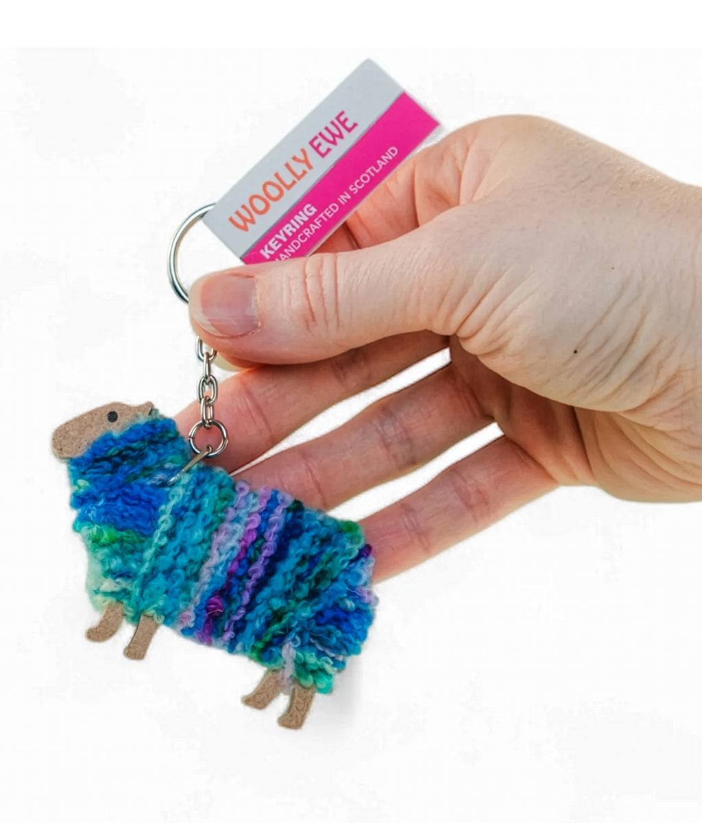 Hand holding a colorful sheep keychain with 'Woolly Ewe' packaging.