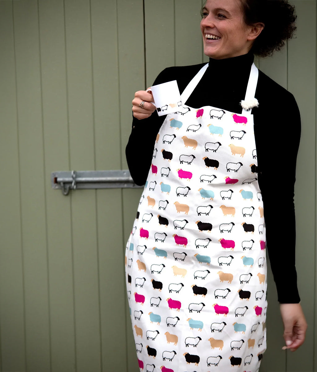 Person wearing a colorful sheep-patterned apron against a green wall.