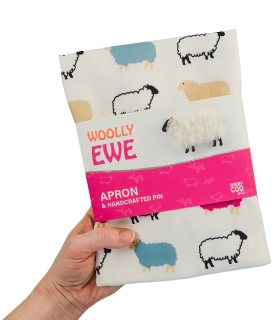 Woolly Ewe apron with sheep pattern held by a hand on a white background