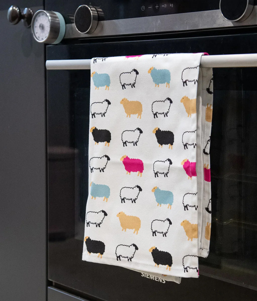Colourful sheep-patterned tea towel hanging on a kitchen towel rack.