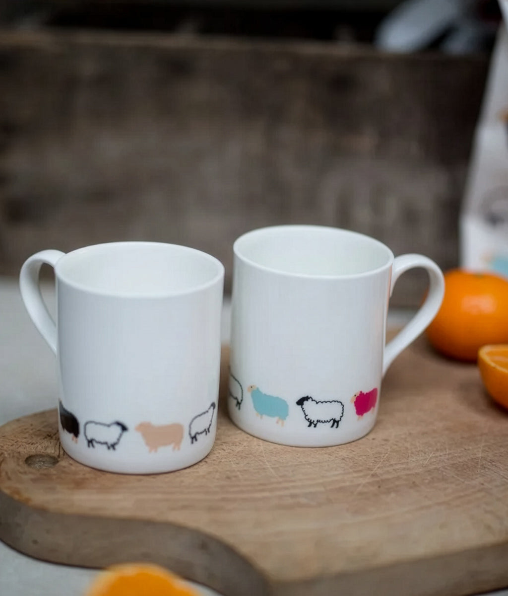 Two white mugs with Woolly Ewe sheepillustrations on a wooden surface.