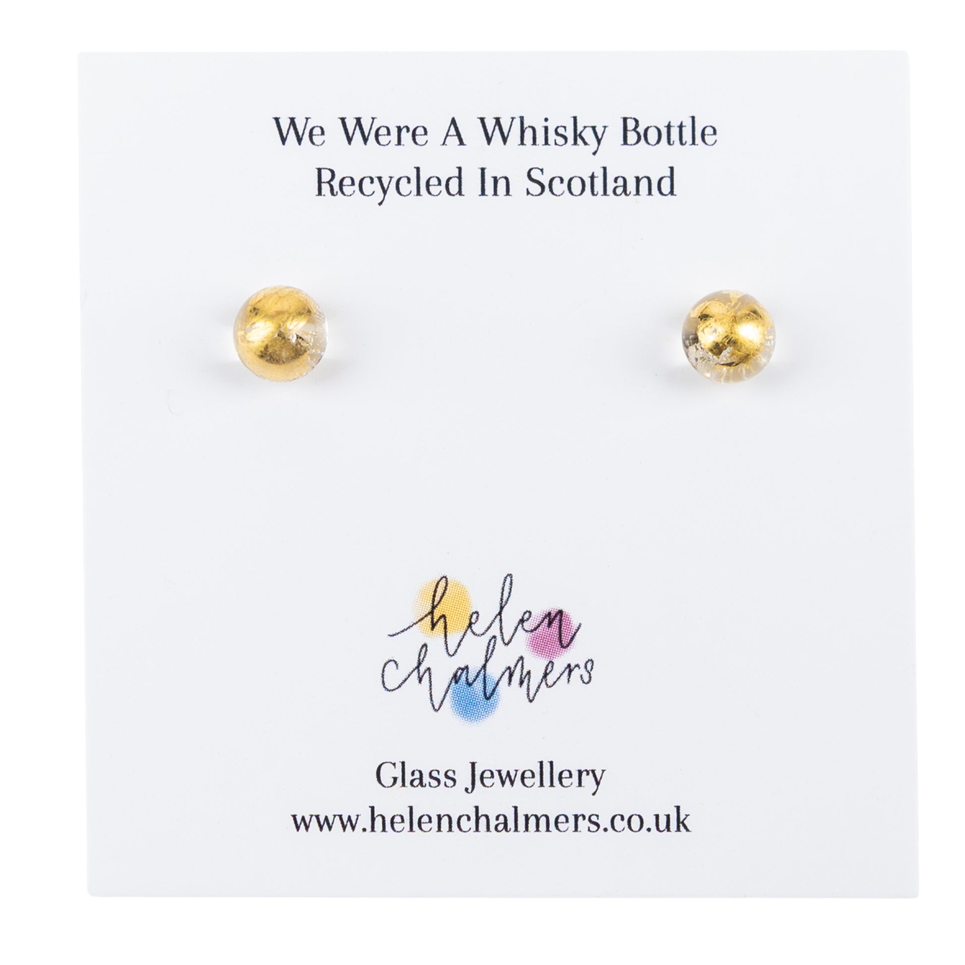 A pair of recycled whisky bottle clear glass and gold stud earrings displayed on a white backing card. The card reads 'We Were A Whisky Bottle Recycled In Scotland' and shows the Helen Chalmers glass jewellery branding.