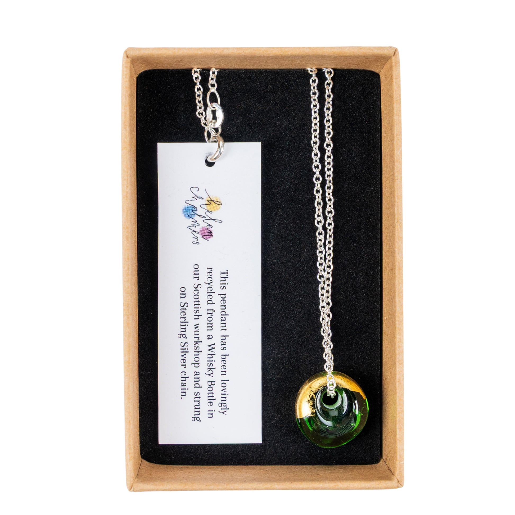 A recycled whisky bottle green glass and gold pendant on Sterling Silver Chain, presented inside a light brown gift box with a black lining and a white product tag.