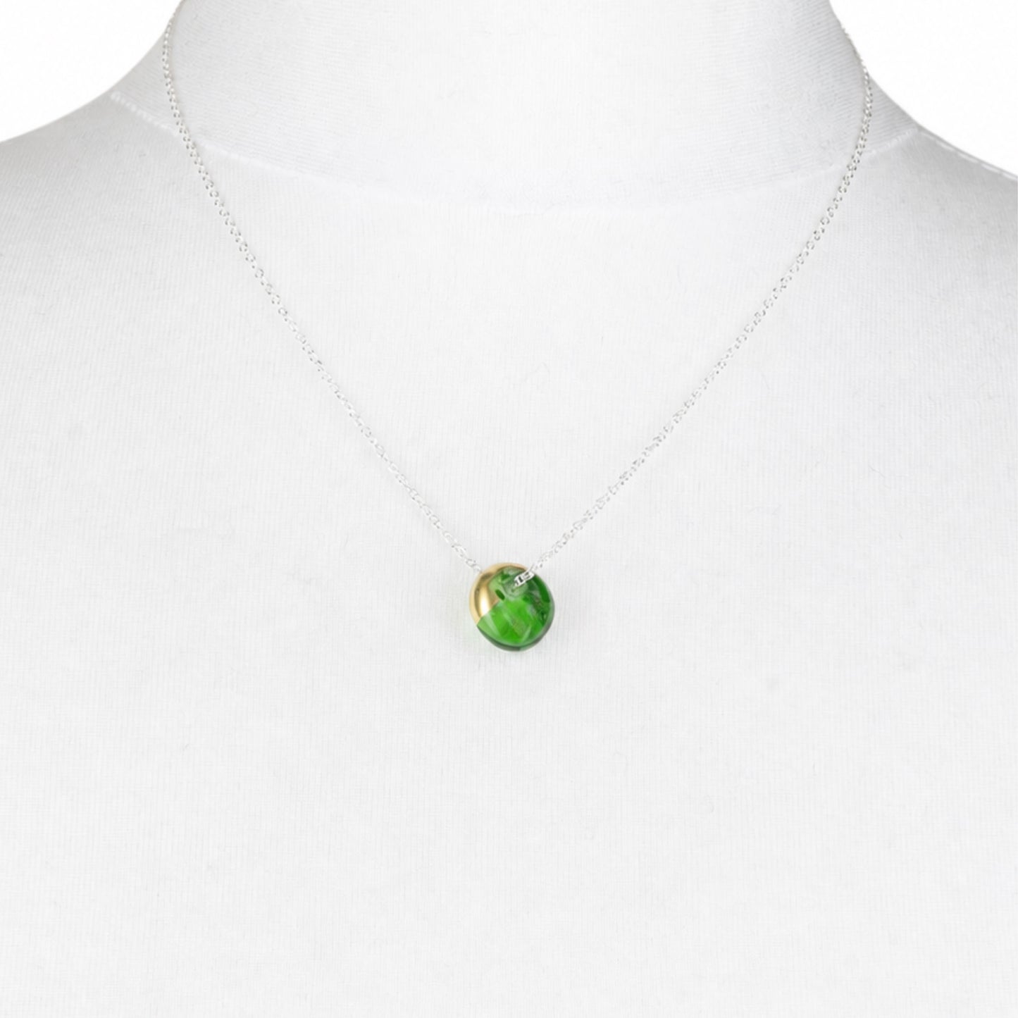 A delicate silver chain necklace with a small round green marbled pendant, displayed on a white mannequin bust.
