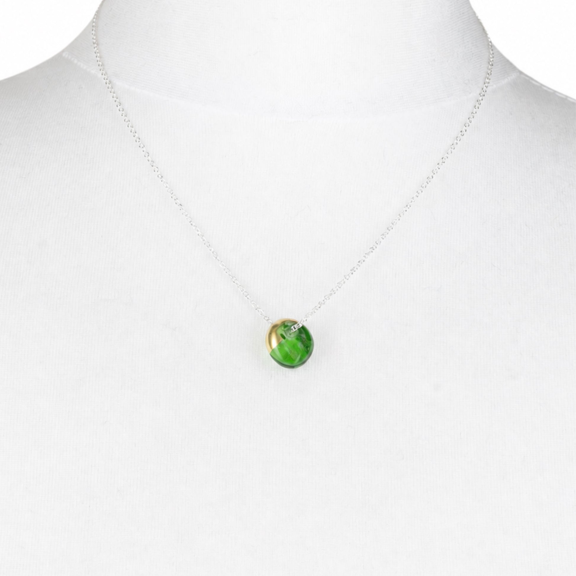 A delicate silver chain necklace with a small round green marbled pendant, displayed on a white mannequin bust.