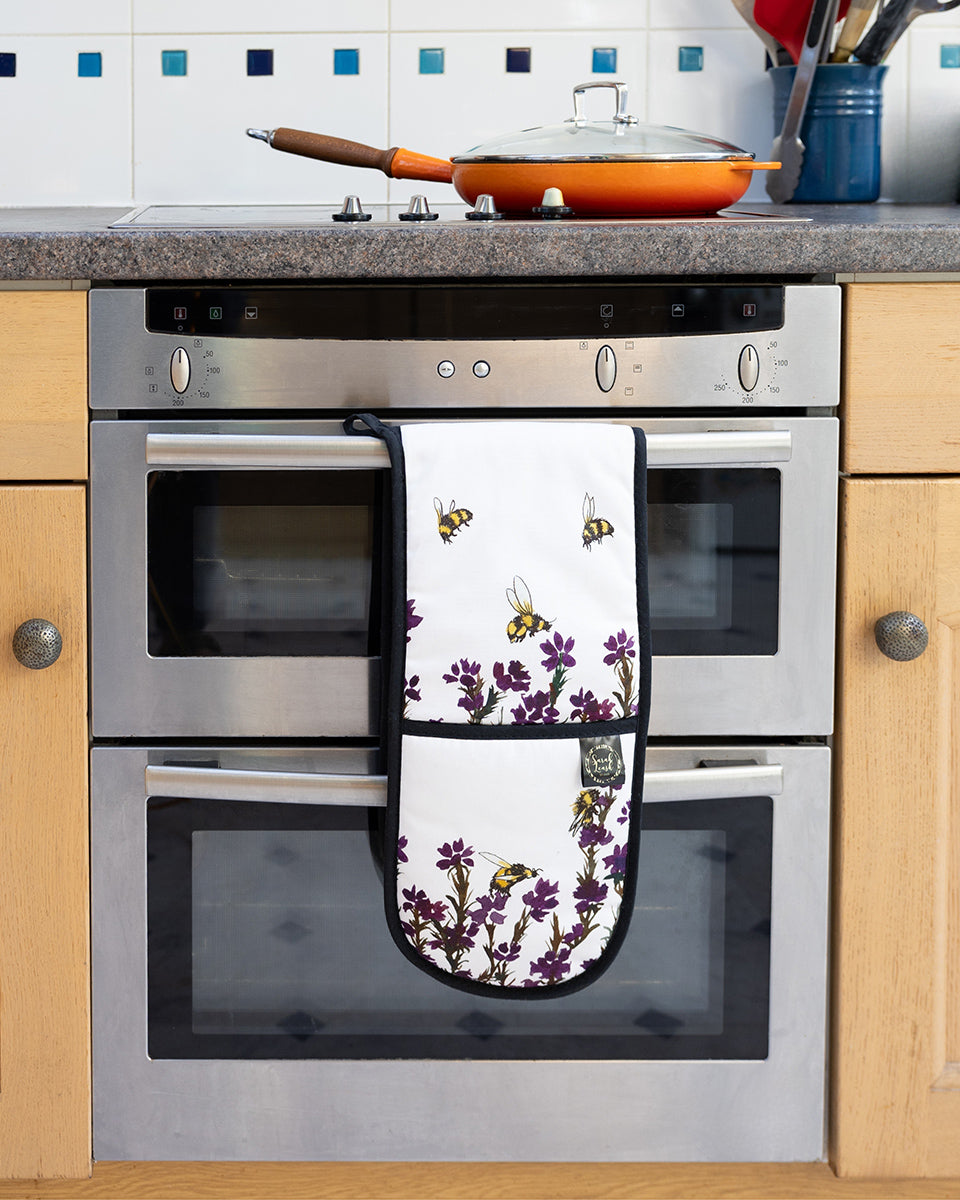 Heather & Honey Oven Gloves by Sarah Leask hanging on an oven door