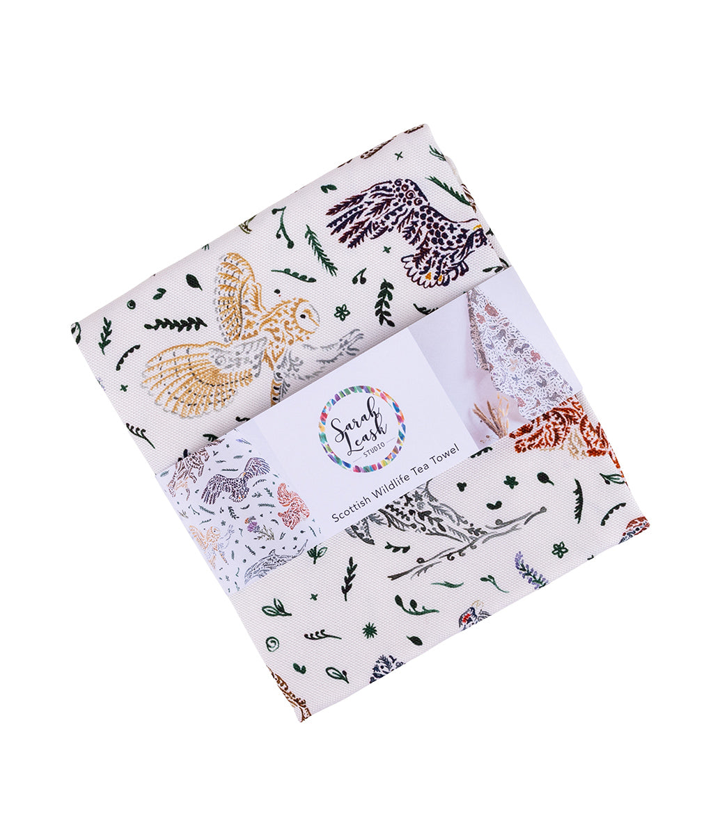 Packaged Wildlife Tea Towel by Sarah Leask featuring patterned fabric with animals and plants on a white background