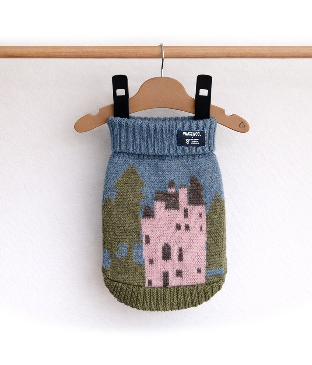 Knitted dog sweater with Craigievar castle design on a hanger against a white background