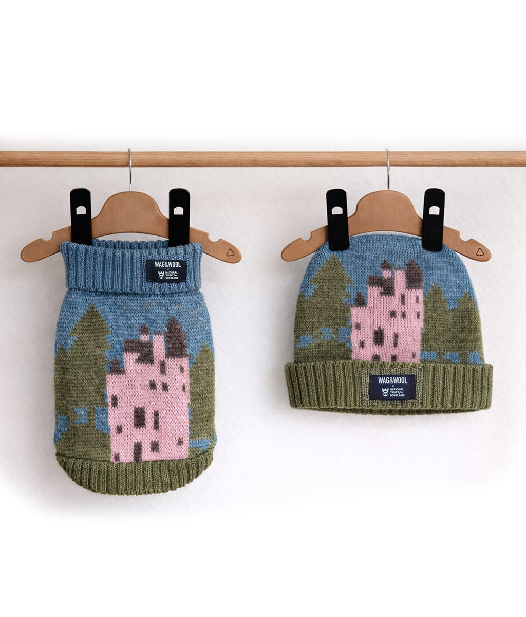 Knitted dog sweater and hat with Craigievar castle design on hangers against a white background