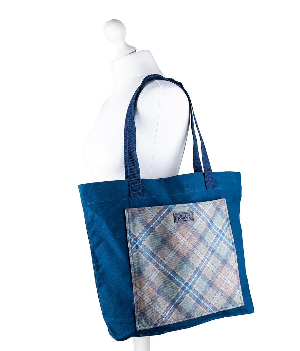Blue tote bag with plaid pocket on a mannequin against a white background