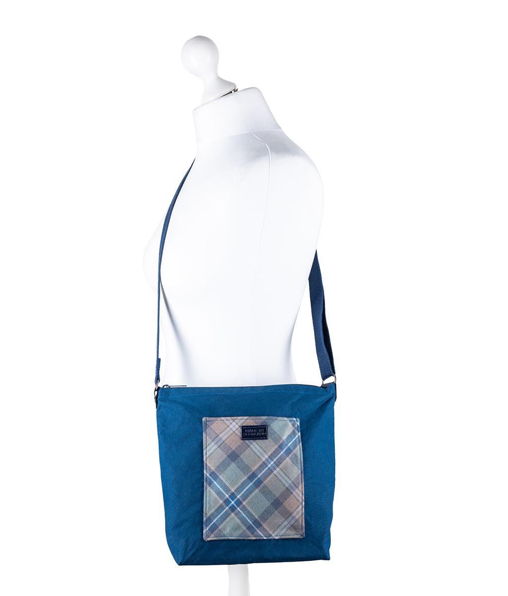 Blue crossbody bag with plaid patch on a mannequin against a white background