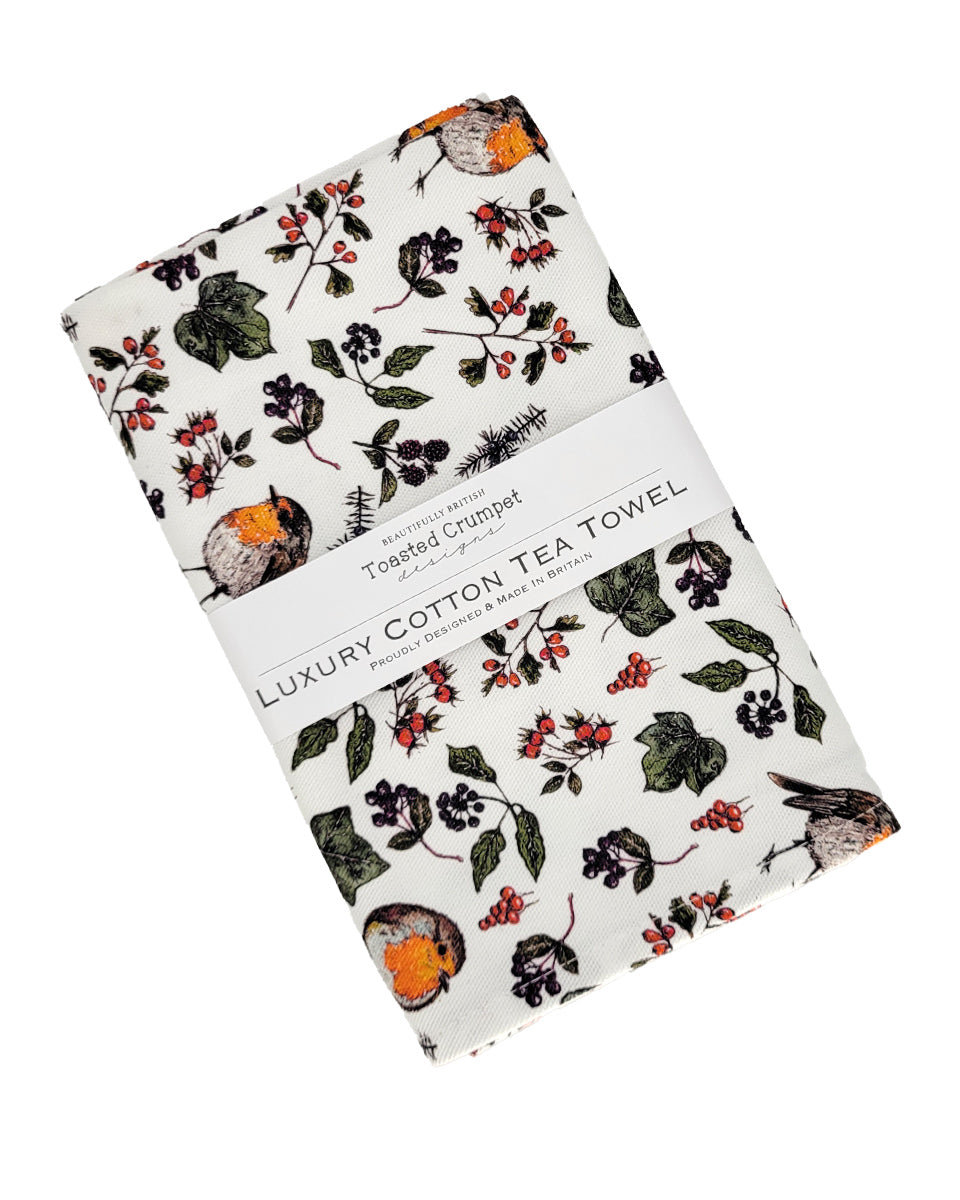 A folded cotton tea towel with a botanical and bird pattern, wrapped in a white paper band labeled 'Luxury Cotton Tea Towel' by Toasted Crumpet.