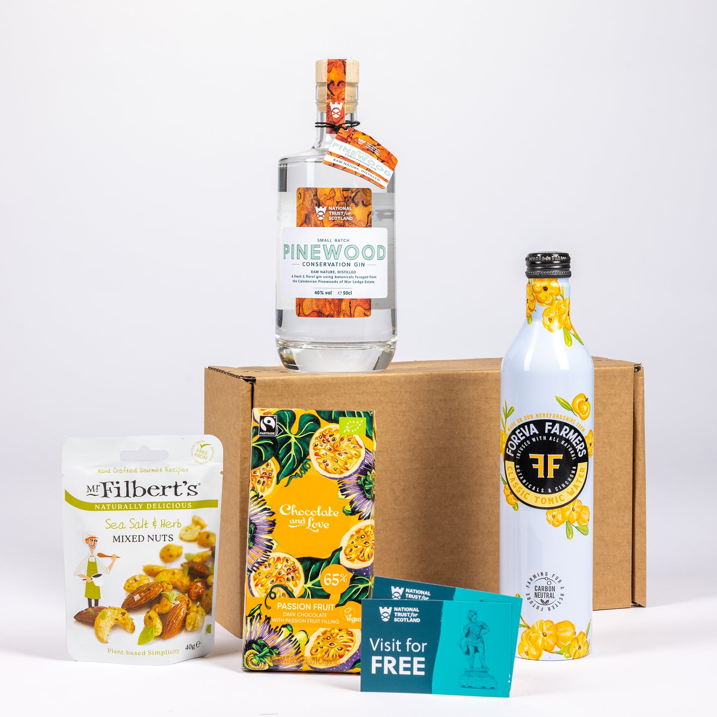 A curated gift set featuring a bottle of Pinewood Gin, arranged in front of a brown cardboard box on a white background.