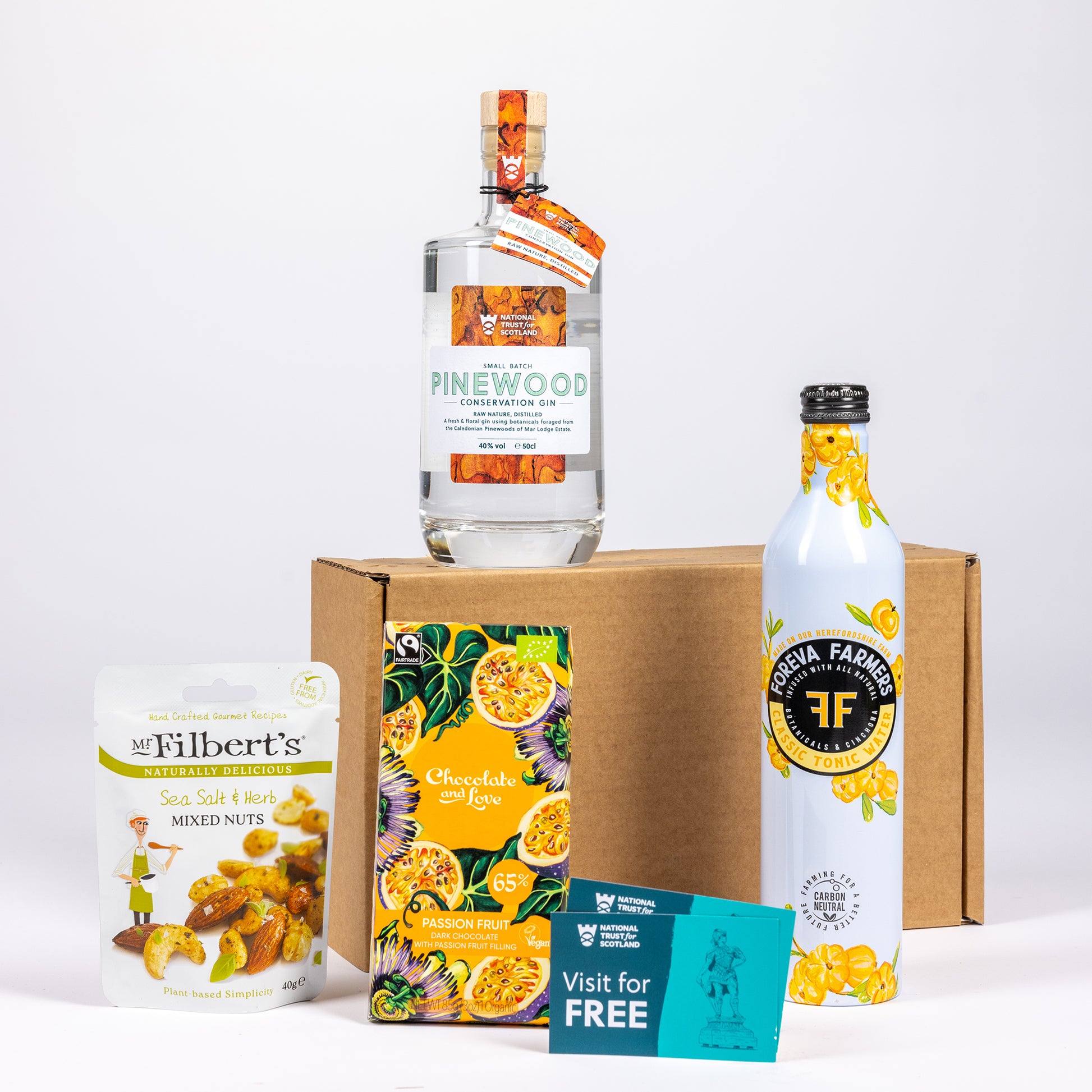 A curated gift set featuring a bottle of Pinewood Gin, arranged in front of a brown cardboard box on a white background.