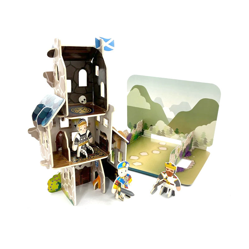 A children's cardboard building and knight puzzle set on a white background, featuring a partially assembled multi-level castle with a small flag, a scenic landscape backdrop, and three small historical figures.