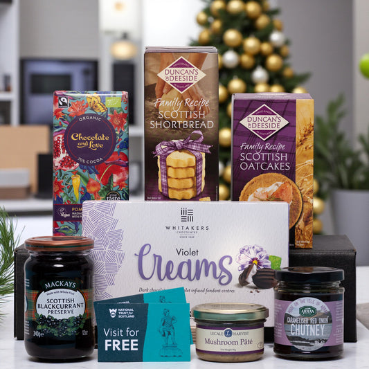 Assorted food products including boxes of Scottish shortbread, oatcakes, and preserves with a Christmas tree in the background.