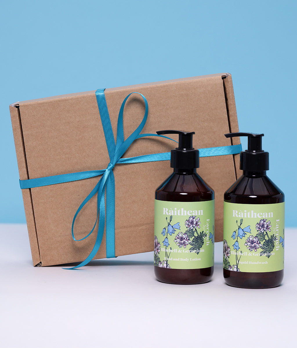 Two bottles of 'Raithean' Spring with floral labels next to a brown gift box tied with teal ribbon on a light blue background.