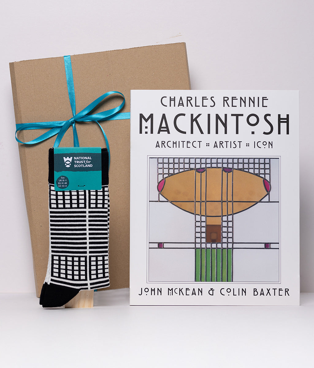 Book titled 'Charles Rennie Mackintosh' with a pair of socks and a gift box on a white background