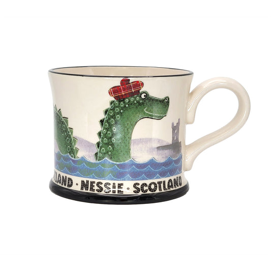 Mug with a design of a green creature, likely a Nessie, wearing a red hat with Scotland text on a white background.
