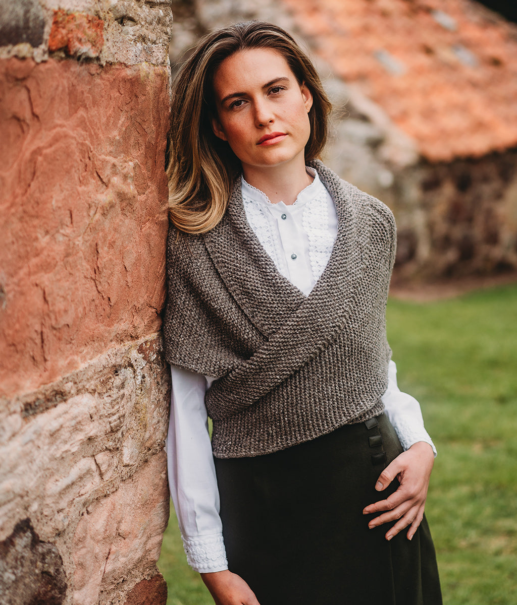 Woman wearing a Merino Wool Sontag Shawl against a stone wall and grass background