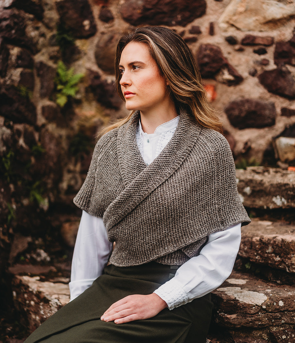 Woman wearing a Merino Wool Sontag Shawl against a stone wall and grass background
