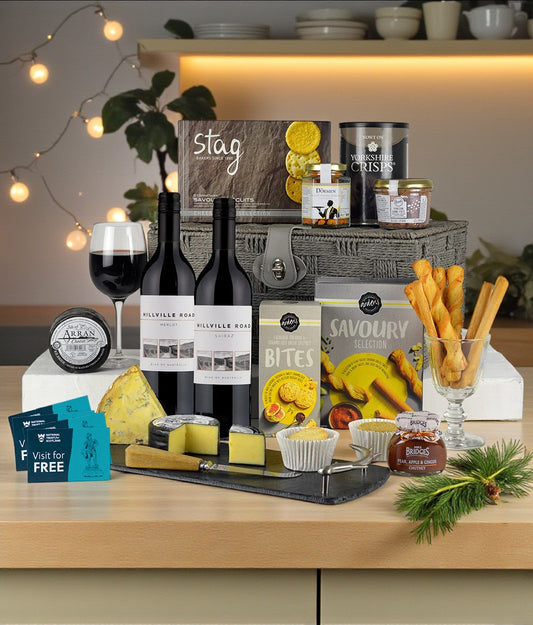 Gourmet gift set with wine, cheese, and snacks on a wooden table.