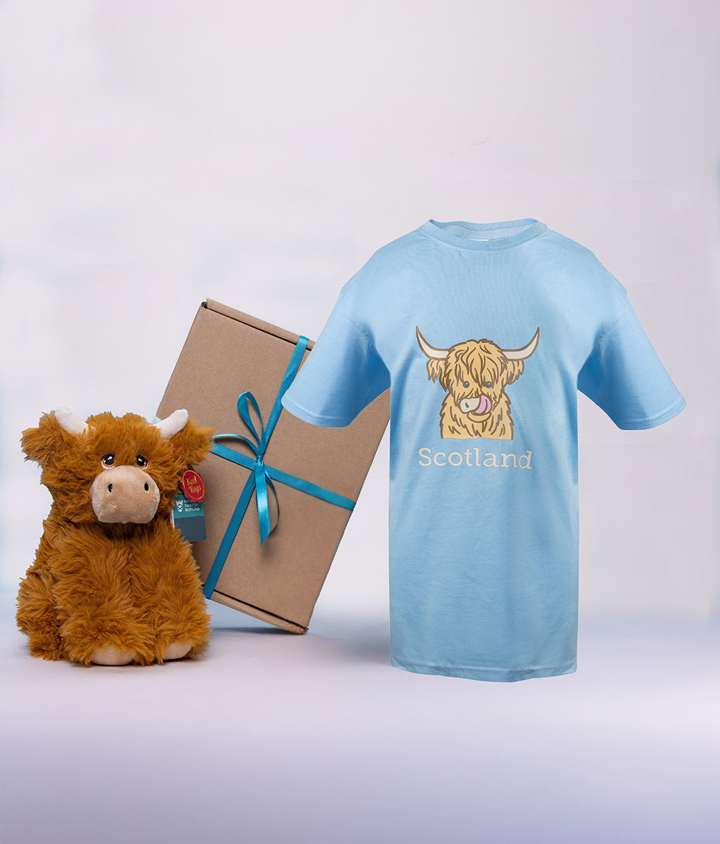 Blue t-shirt with a highland cow design and 'Scotland' text, plush toy highland cow, and gift box on a light gray background