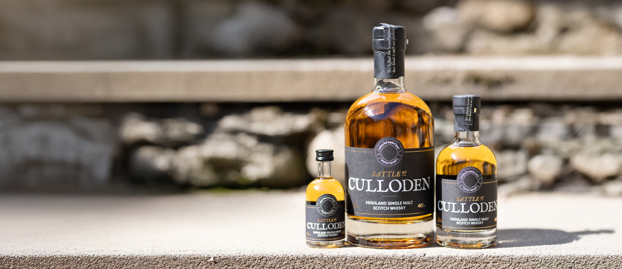 Three bottles of Culloden whiskey on a stone surface with a blurred natural background