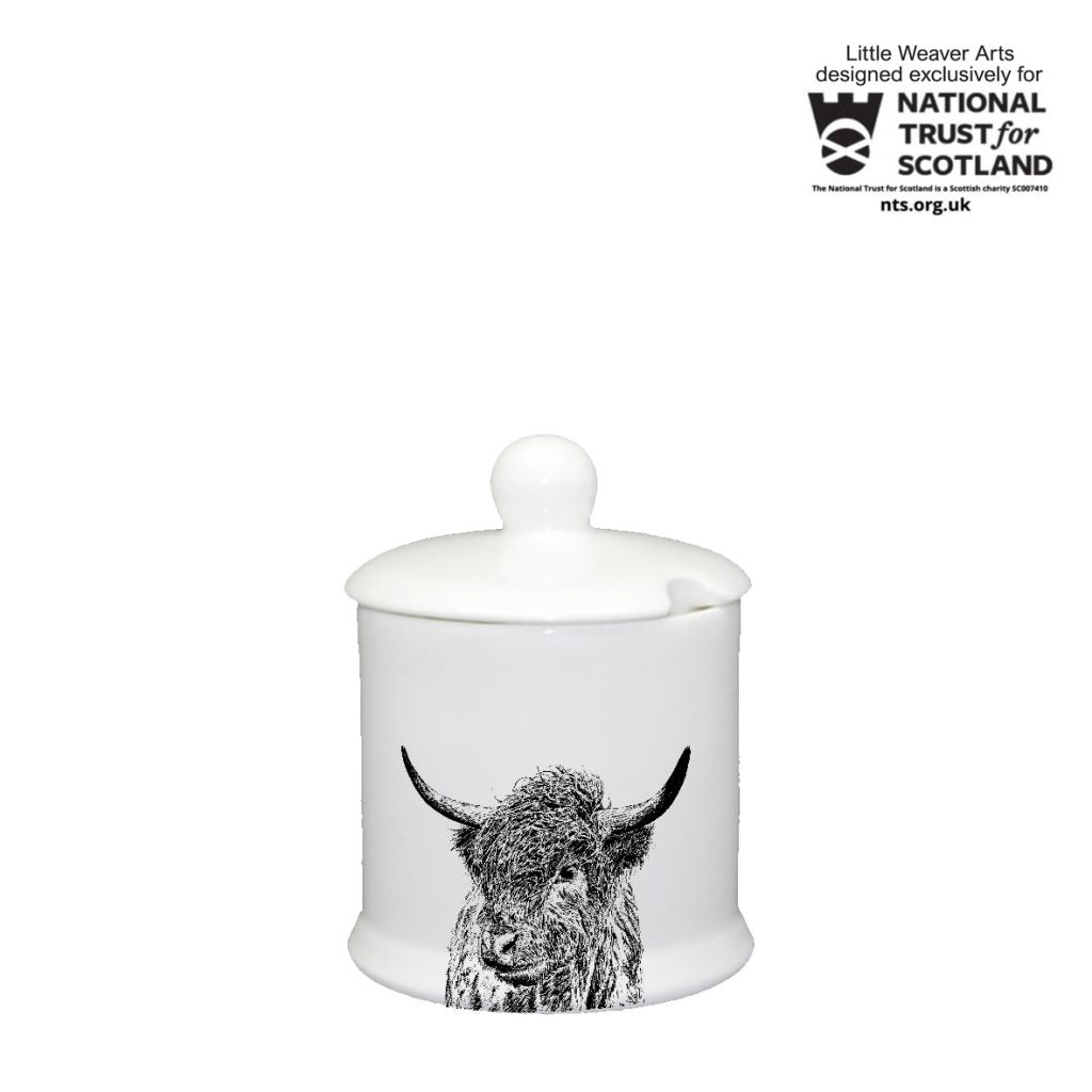 A white ceramic jar with a matching lid and a black-and-white highland cow illustration on the front, shown on a white background. A National Trust for Scotland badge appears in the top right corner.