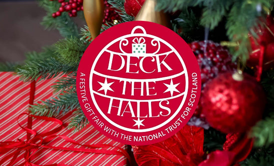 Red and white 'Deck the Halls' sign with Christmas decorations in the background