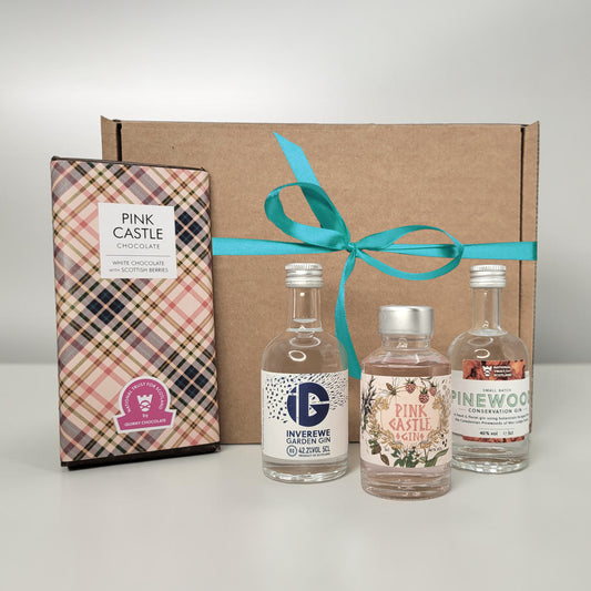 Three miniature gin bottles in a cardboard gift box with a teal ribbon, accompanied by a chocolate box labeled 'Pink Castle'.