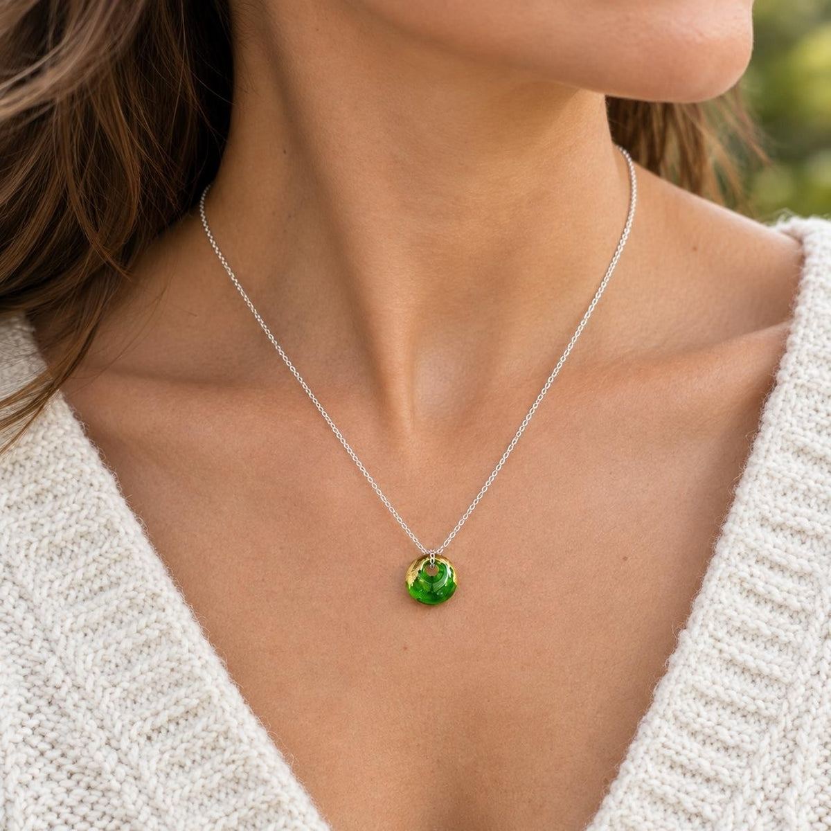 A close-up of a woman wearing a delicate silver chain necklace with a small, round, vibrant green faceted pendant.