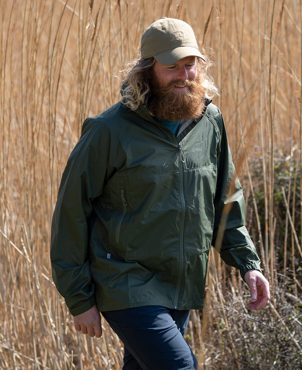 Man wearing a Keela 'Where Nature Leads' packaway jacket and beige cap walking through tall reeds.