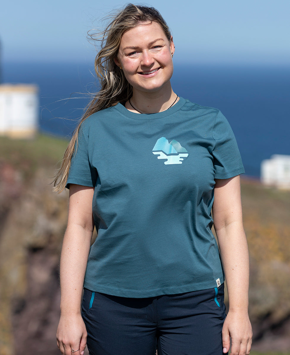 Woman wearing a teal Keela Women's St Kilda T-Shirt with a logo, standing outdoors with a blurred background
